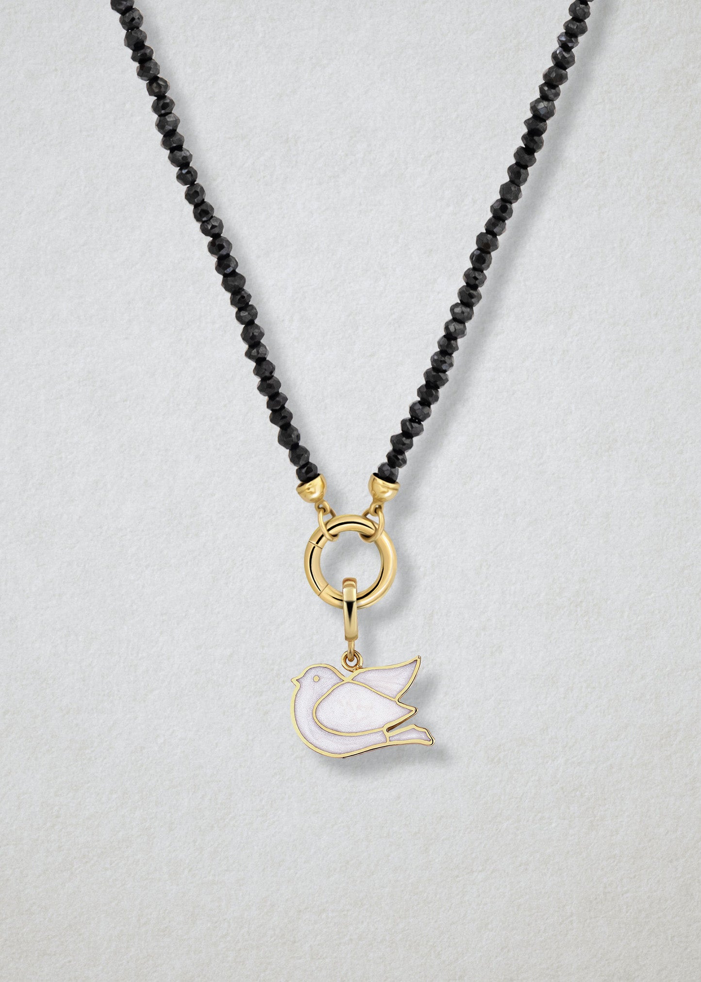 Close-up of the Noir Elegance Dove of Hope Charm Necklace, featuring faceted black spinel beads, a golden link charm holder, and a dove of hope charm with white enamel by whywhy NYC