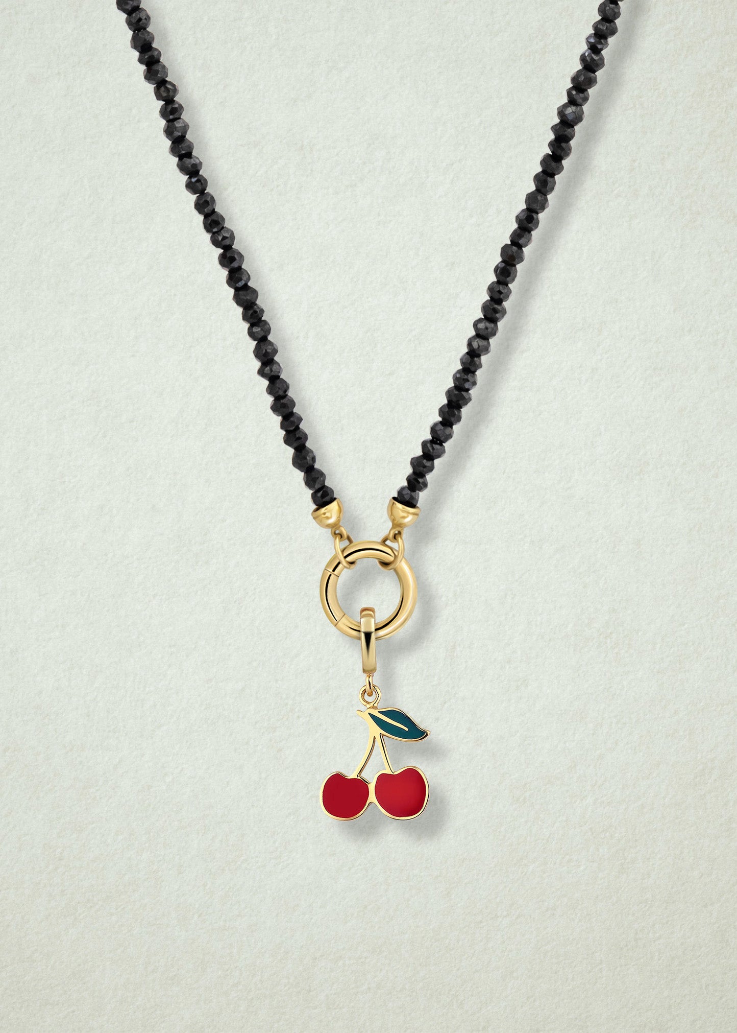 Close-up of the Noir Elegance Cherry on Top Charm Necklace, featuring faceted black spinel beads, a golden link charm holder, and a cherry on top charm with red enamel by whywhy NYC.