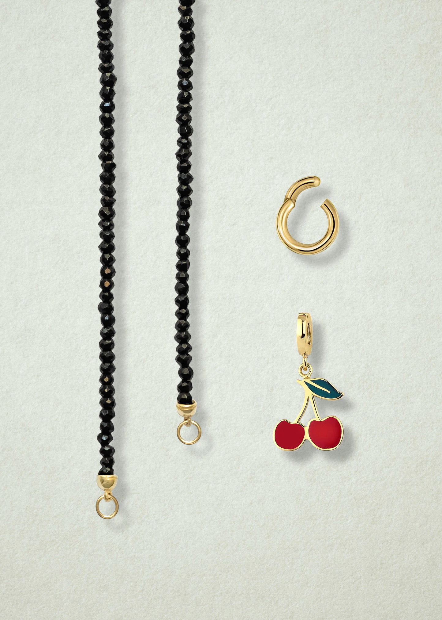 Close-up of the separated Noir Elegance Cherry on Top Charm Necklace components: black spinel necklace, golden link charm holder, and cherry on top charm with red enamel by whywhy NYC.