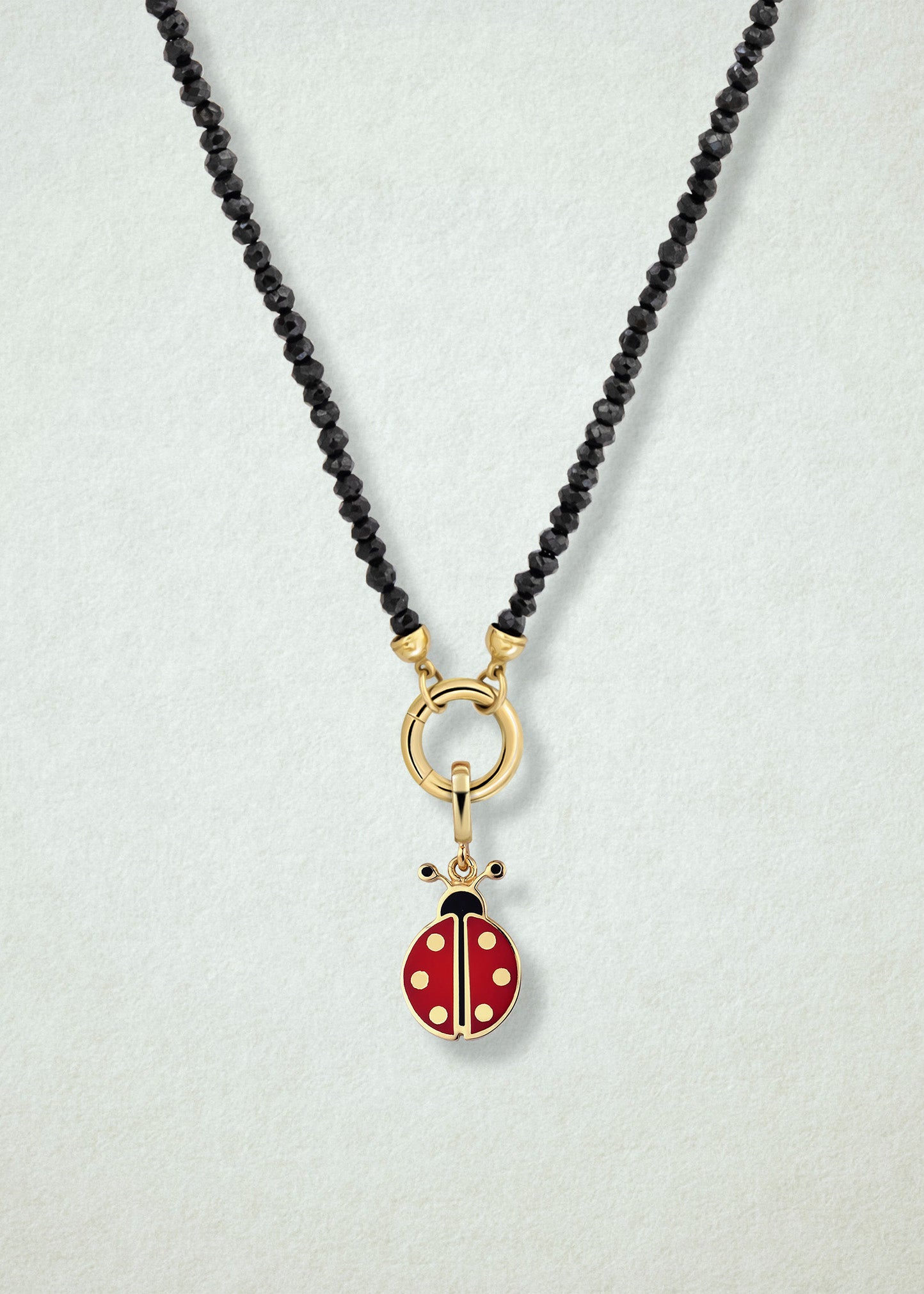 Close-up of the Noir Elegance Lucky Clover Charm Necklace, featuring faceted black spinel beads, a golden link charm holder, and a lucky clover charm with green enamel by whywhy NYC.