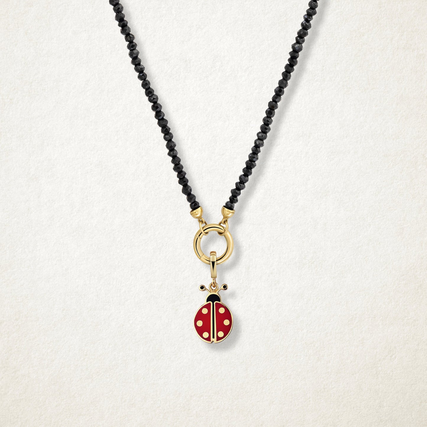 Close-up of the Lucky Ladybird Charm with red and black enamel on the Noir Elegance black spinel bead necklace, shown on a soft light background.