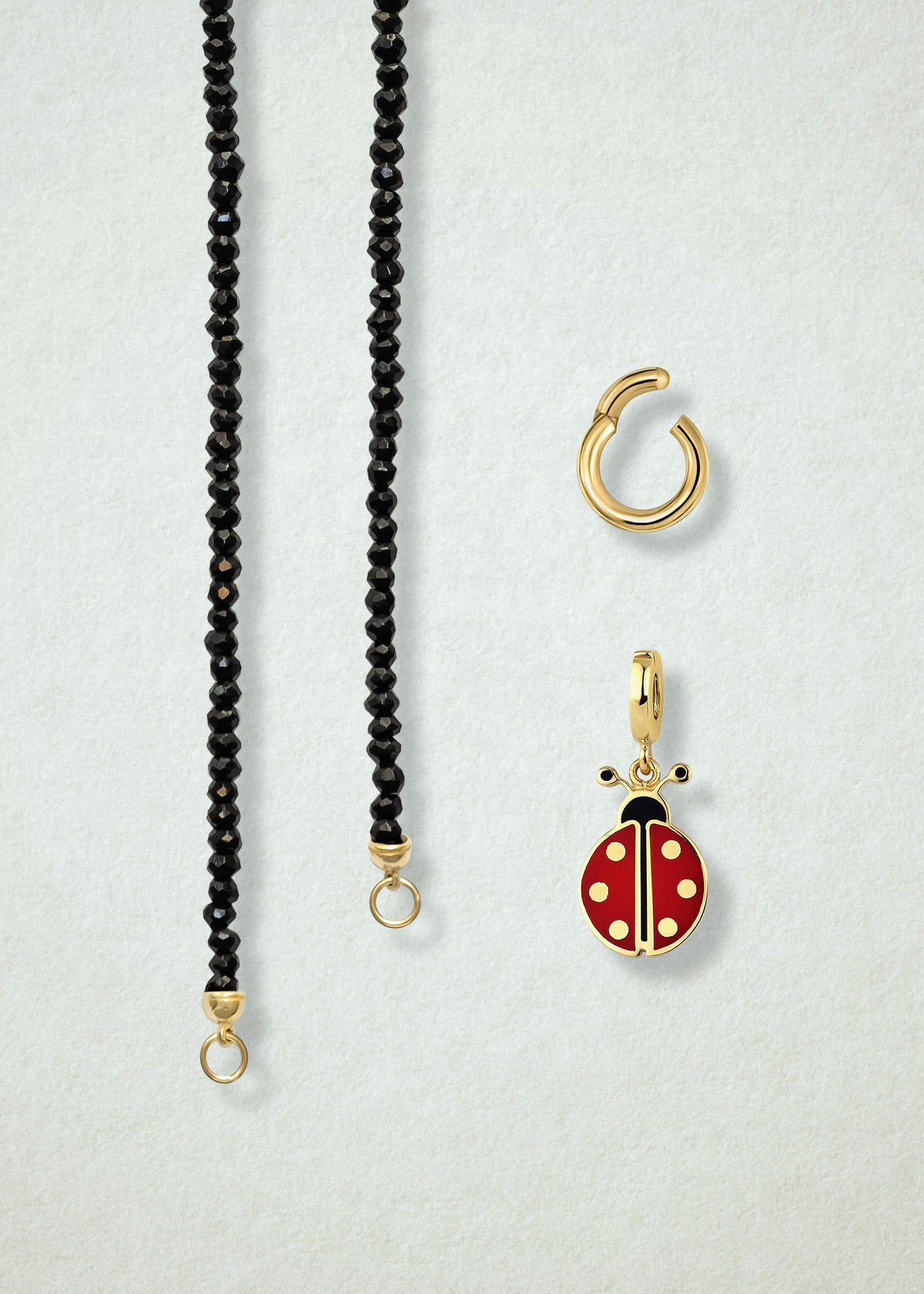 Close-up of the separated Noir Elegance Lucky Clover Charm Necklace components: black spinel necklace, golden link charm holder, and lucky clover charm with green enamel by whywhy NYC.