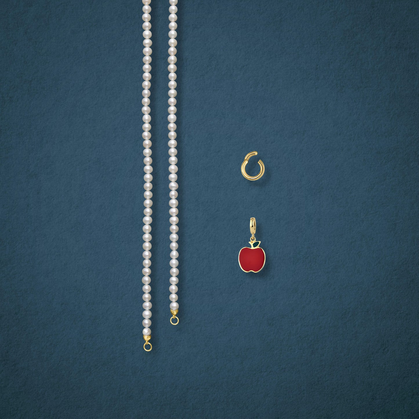 Separated components of the Lustrous Pearl Golden Apple of NYC Charm Necklace, including pearl necklace, charm holder, and golden apple charm in 14K solid gold by whywhy NYC.