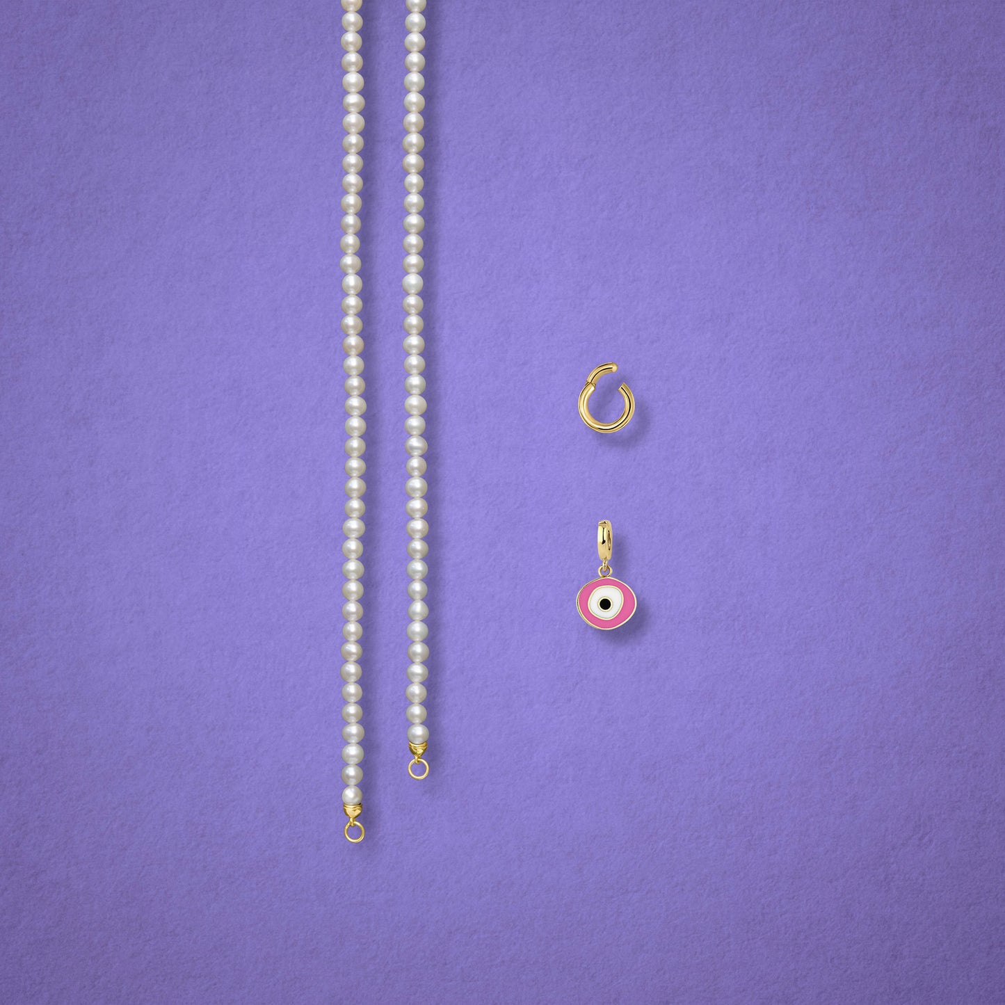 Blush Organic Evil Eye Charm, Golden Link Charm Holder, and the Lustrous Pearl necklace displayed separately on a lilac background to show styling options.