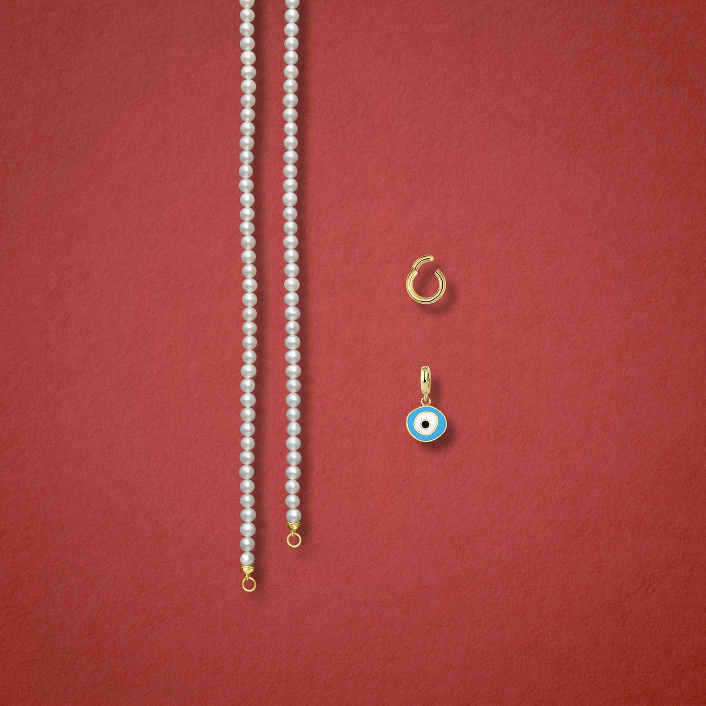 Sky Organic Evil Eye Charm, Golden Link Charm Holder, and Lustrous Pearl necklace are displayed separately on a red background to showcase styling options.