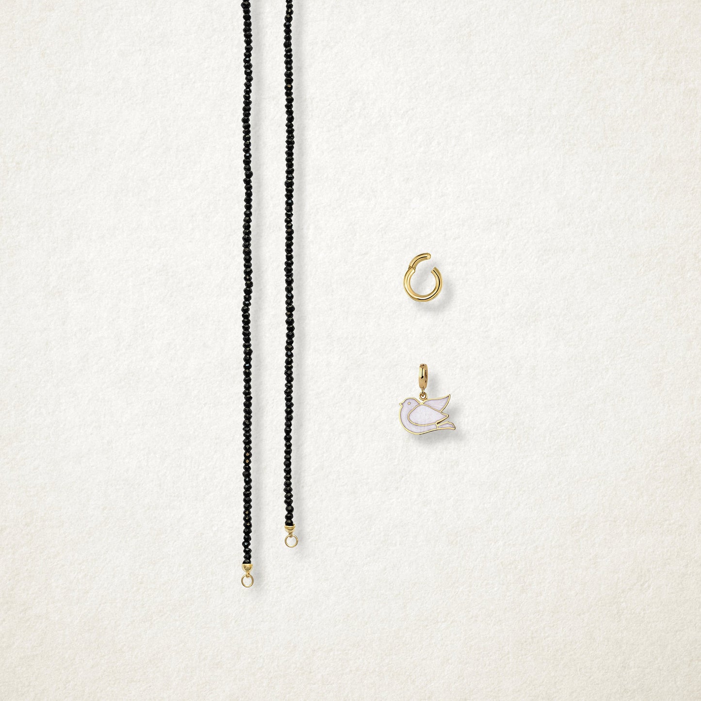 Separated components of the Noir Elegance Dove of Hope Charm Necklace, including black spinel necklace, golden link charm holder, and dove of hope charm with white enamel by whywhy NYC.