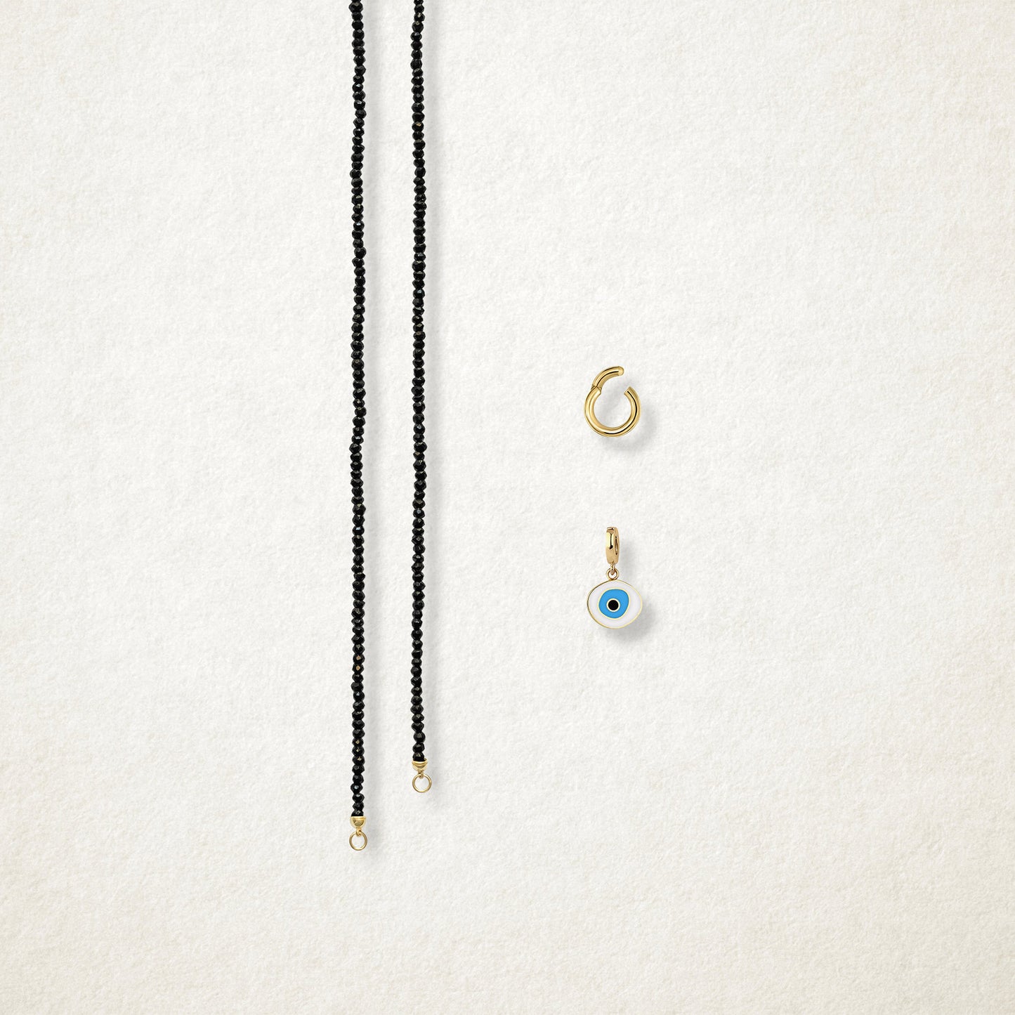 Azure Organic Evil Eye Charm and the Noir Elegance black spinel necklace displayed separately on a soft light background to show styling options.