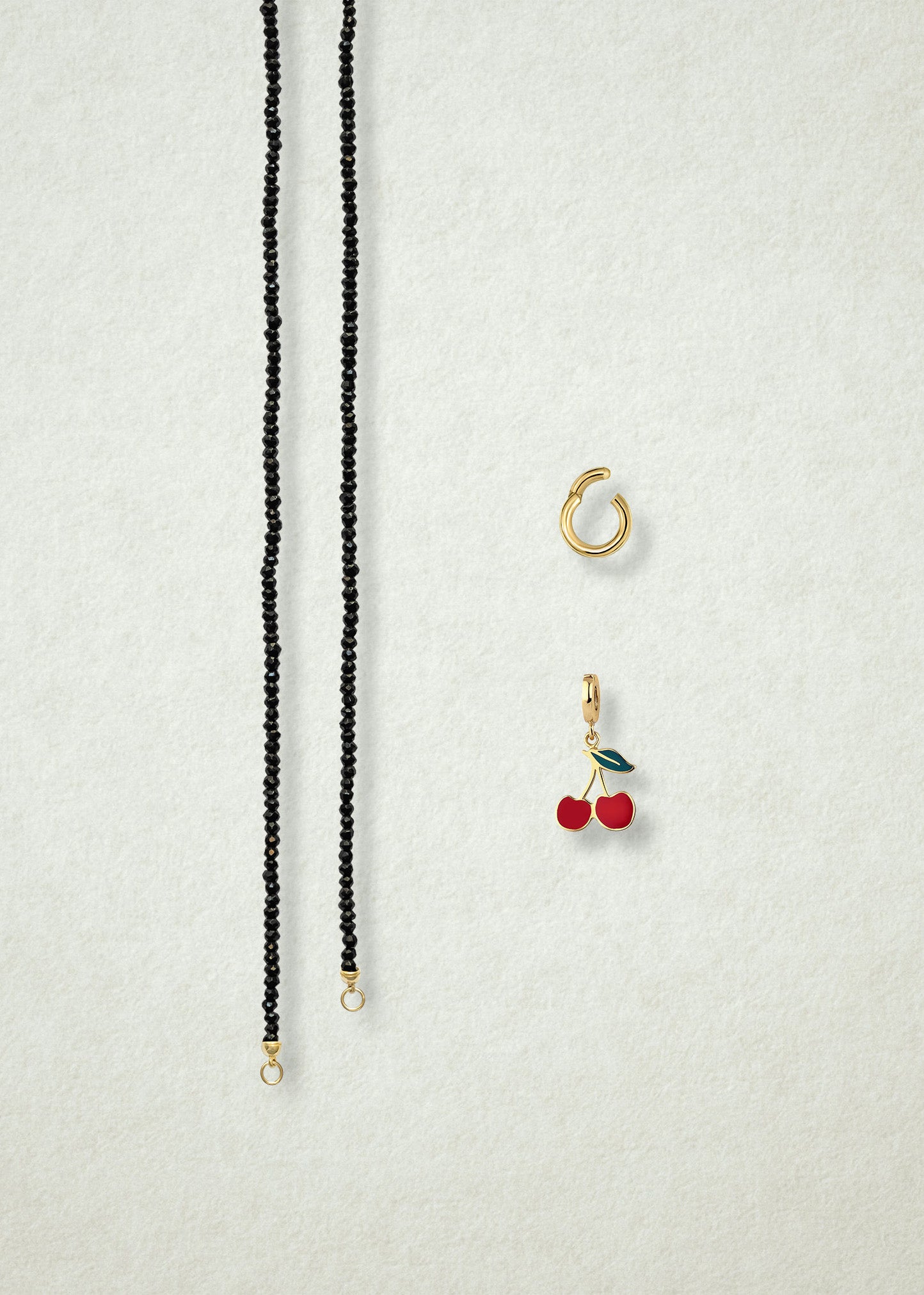 Separated components of the Noir Elegance Cherry on Top Charm Necklace, including black spinel necklace, golden link charm holder, and cherry on top charm with red enamel by whywhy NYC.