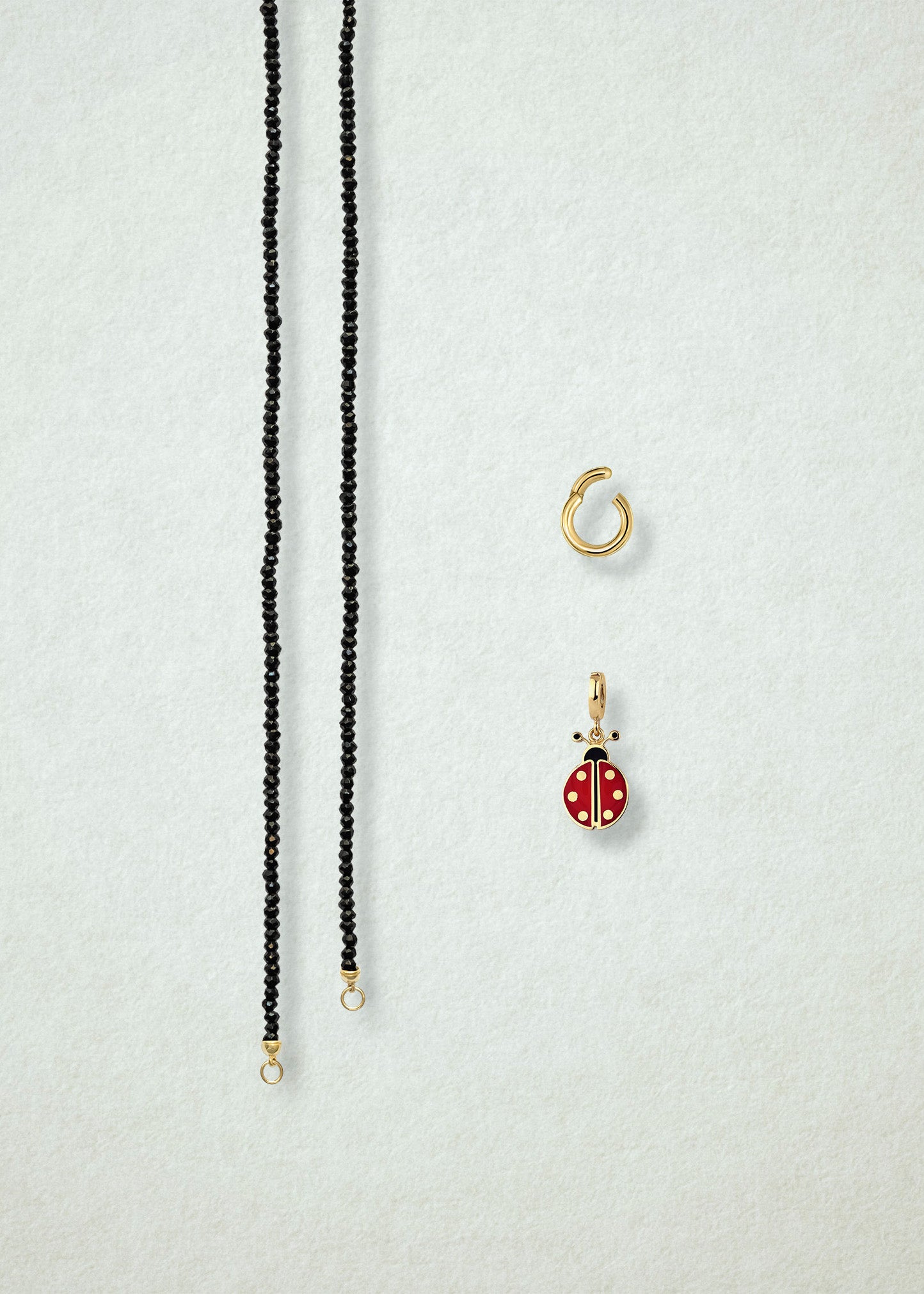 Separated components of the Noir Elegance Lucky Clover Charm Necklace, including black spinel necklace, golden link charm holder, and lucky clover charm with green enamel by whywhy NYC.