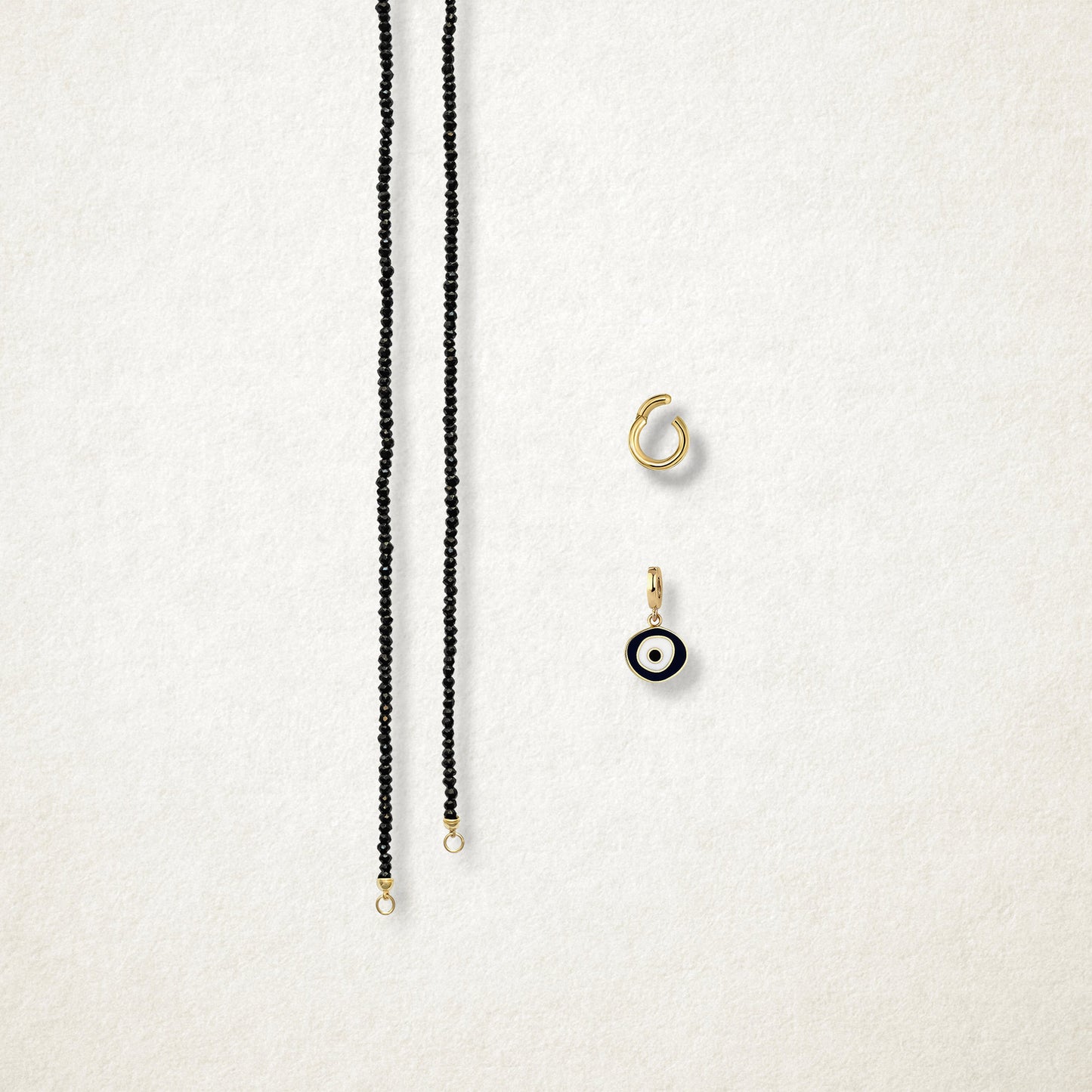Obsidian Organic Evil Eye Charm and the Noir Elegance black spinel necklace displayed separately on a soft light background to show styling options.