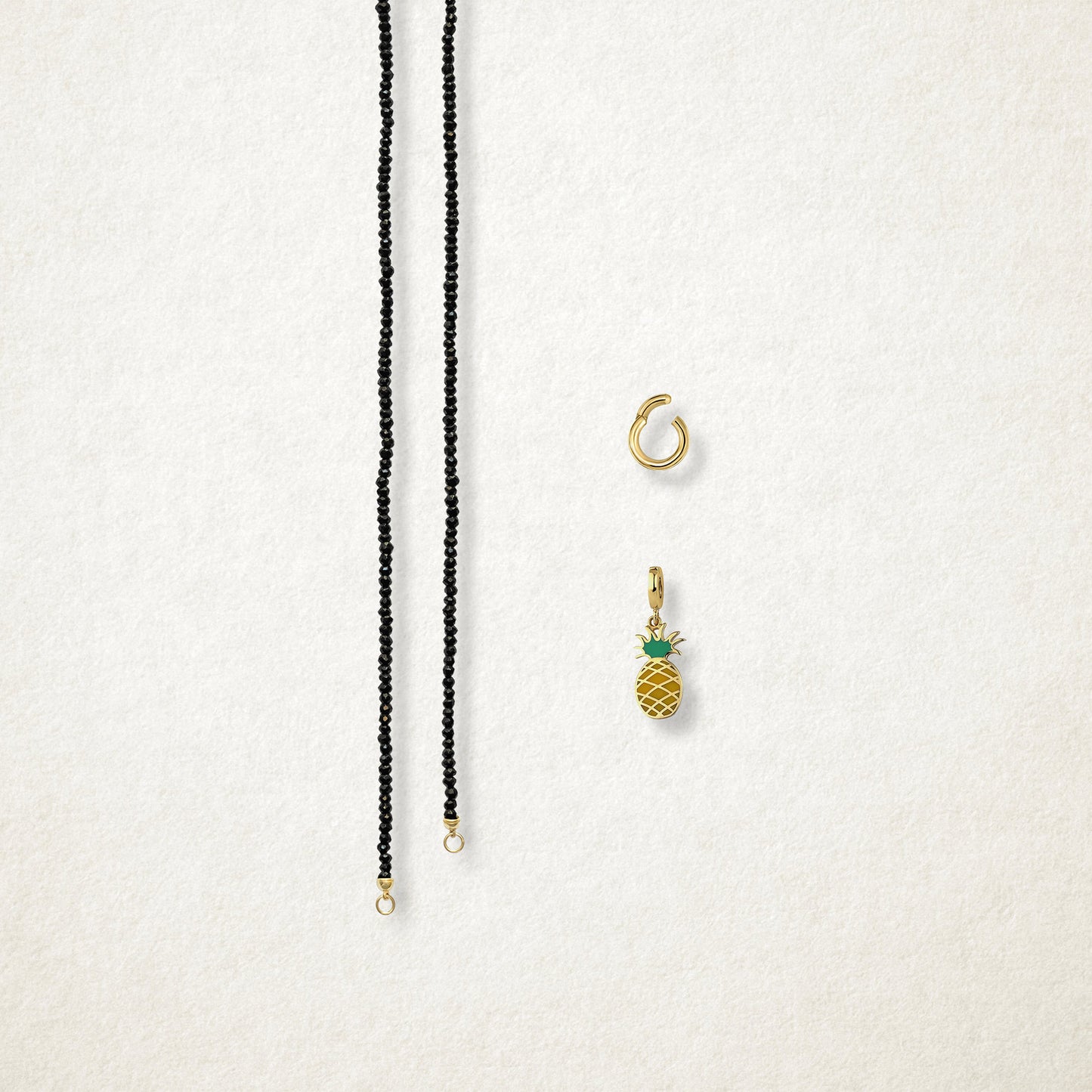 Separated components of the Noir Elegance Pineapple Paradise Charm Necklace, including black spinel necklace, golden link charm holder, and pineapple paradise charm with green enamel by whywhy NYC.