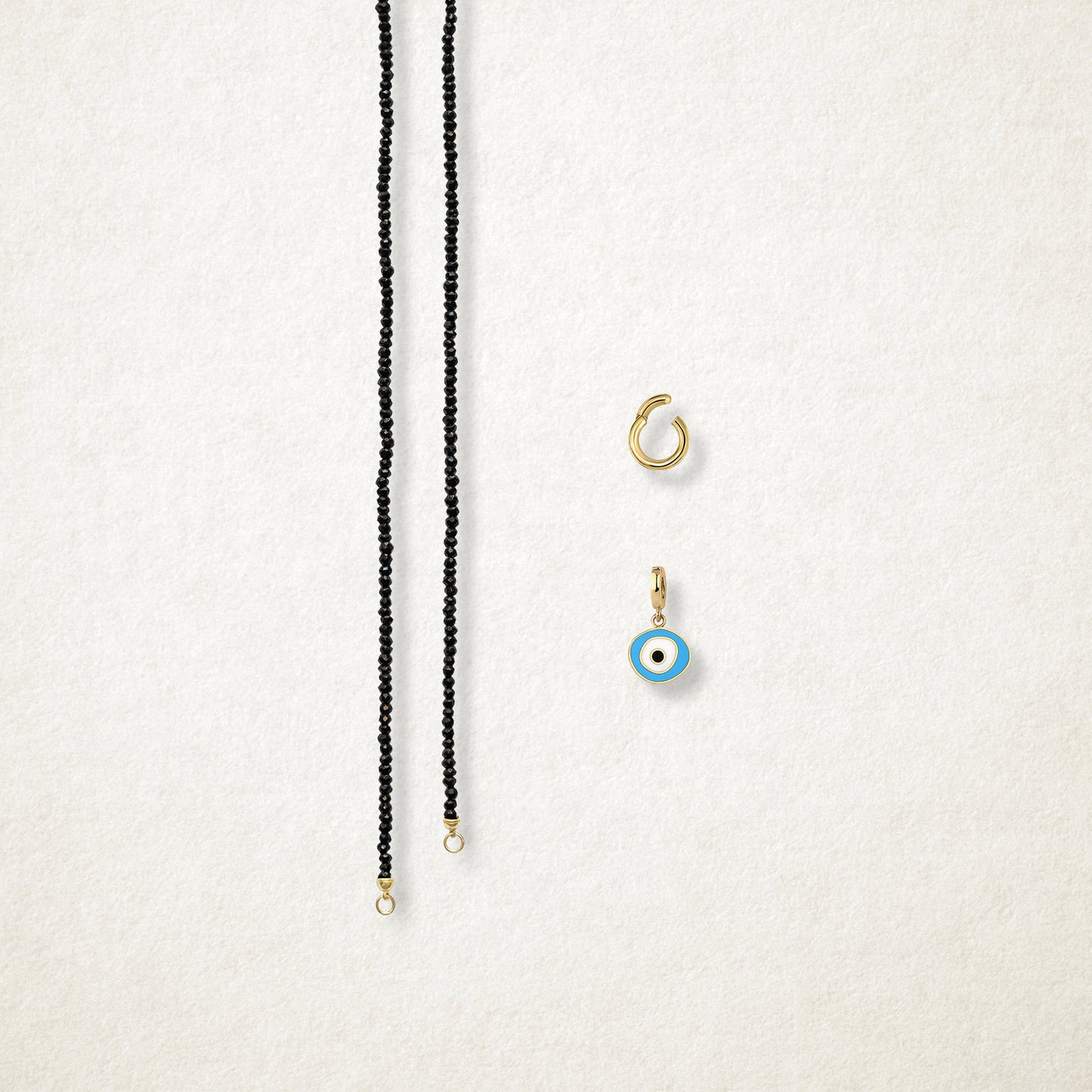 Azure Organic Evil Eye Charm and the Noir Elegance black spinel necklace displayed separately on a soft light background to show styling options.