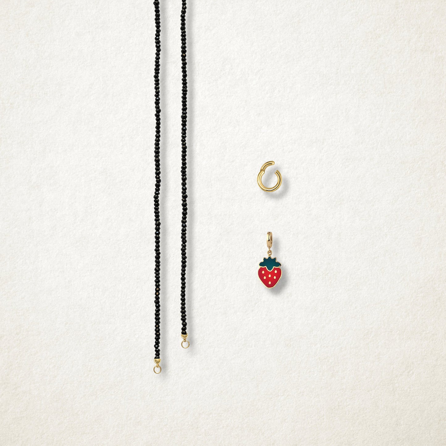 Separated components of the Noir Elegance Sweet Strawberry Charm Necklace, including black spinel necklace, golden link charm holder, and sweet strawberry charm with red enamel by whywhy NYC.