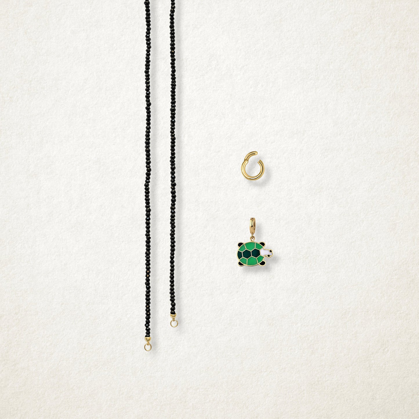 Separated components of the Noir Elegance Turtle Treasure Charm Necklace, including black spinel necklace, golden link charm holder, and turtle treasure charm with green enamel by whywhy NYC.
