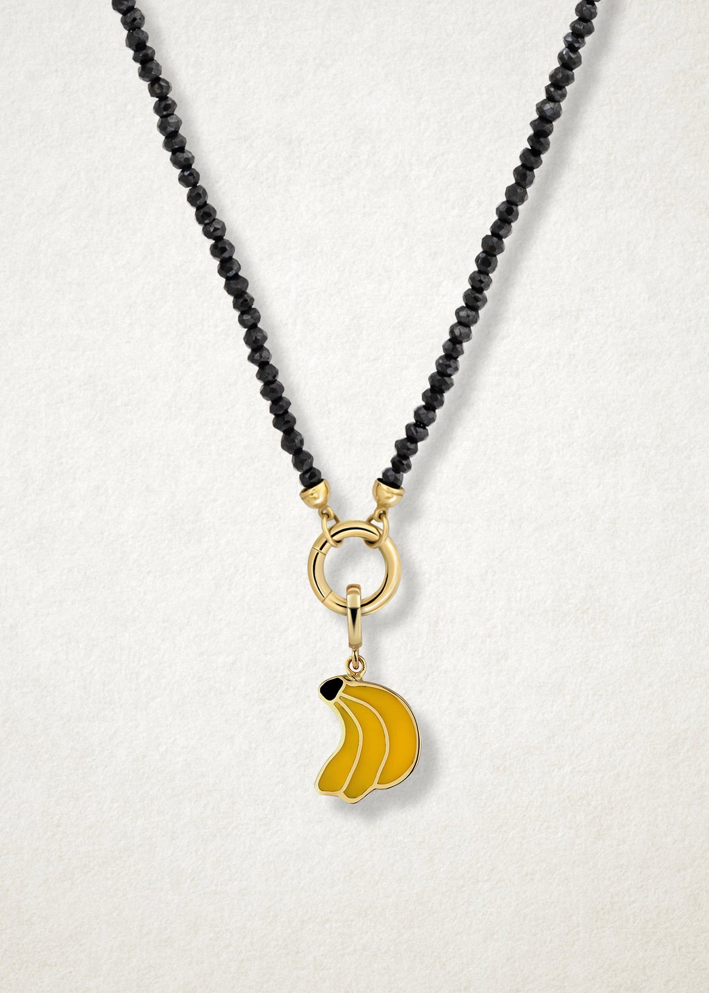 Close-up of the Banana Bliss Charm paired with the Noir Elegance Charm Necklace by whywhy NYC, featuring black spinel and 14K solid gold for a striking and playful look.