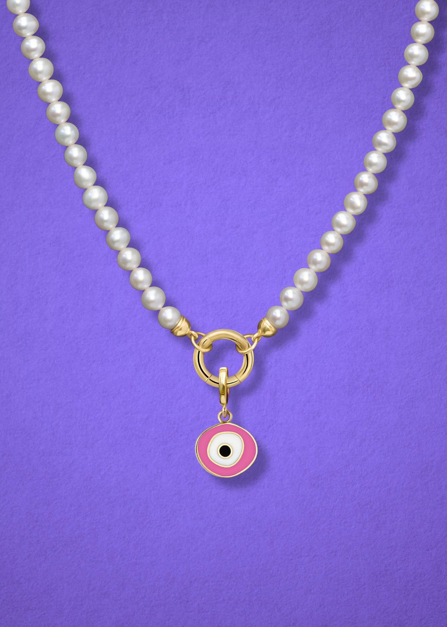 Close-up of the Blush Organic Evil Eye Charm with pink, white, and black enamel on the Lustrous Pearl necklace, shown on a lilac background.