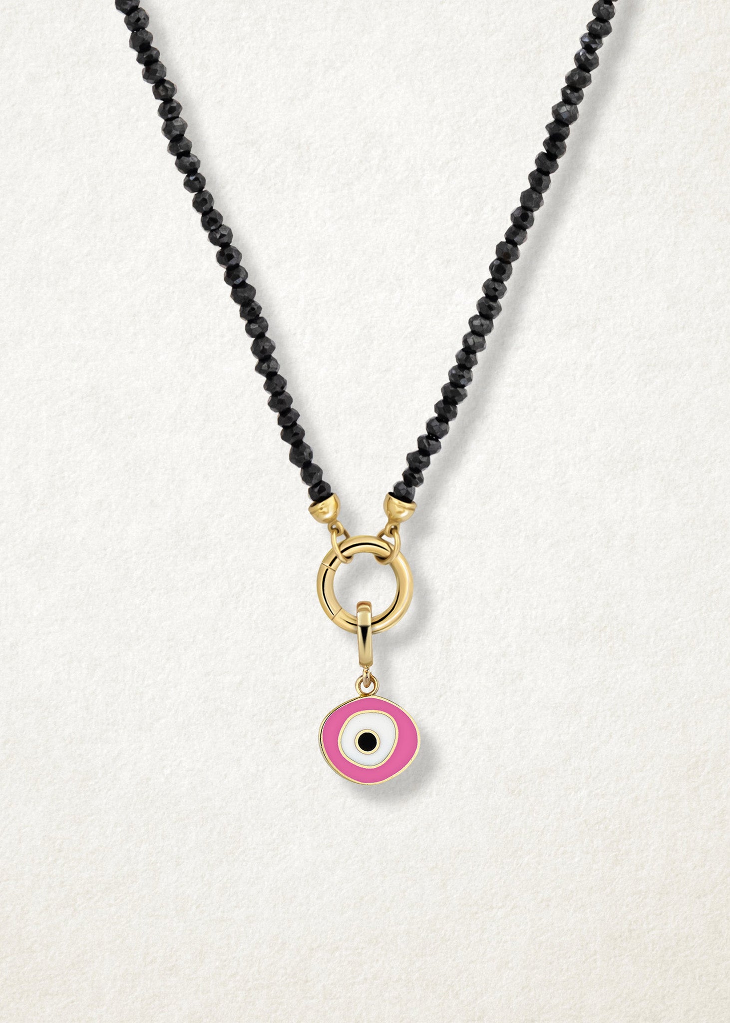 Close-up of the Blush Organic Evil Eye Charm with pink, white, and black enamel on the Noir Elegance black spinel bead necklace, shown on a soft light background.