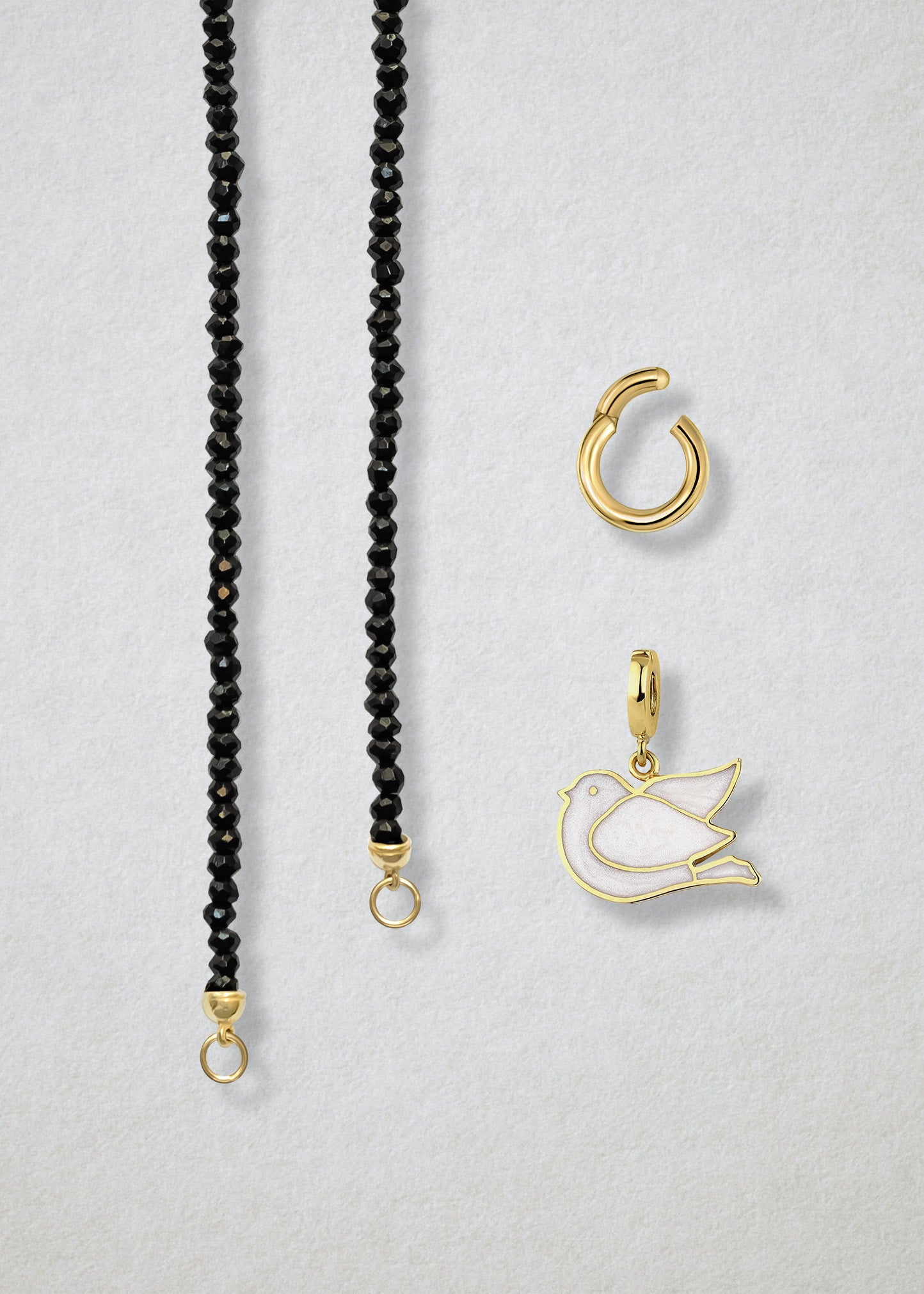 Close-up of the separated Noir Elegance Dove of Hope Charm Necklace components: black spinel necklace, golden link charm holder, and dove of hope charm with white enamel by whywhy NYC.