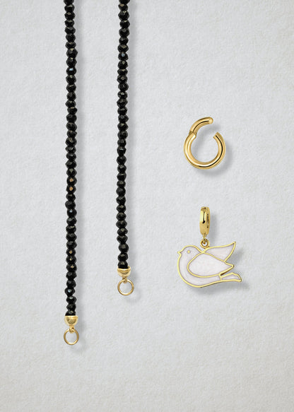 Close-up of the separated Noir Elegance Dove of Hope Charm Necklace components: black spinel necklace, golden link charm holder, and dove of hope charm with white enamel by whywhy NYC.