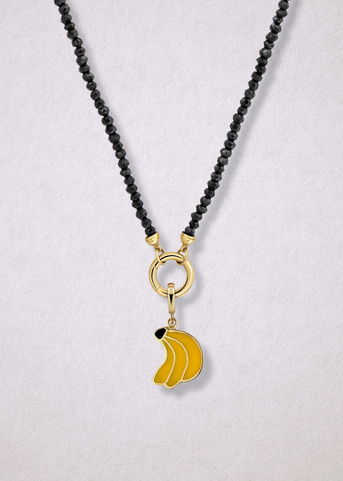 Close-up of the Noir Elegance Banana Bliss Charm Necklace, featuring faceted black spinel beads, a golden link charm holder, and a banana bliss charm with yellow enamel by whywhy NYC.