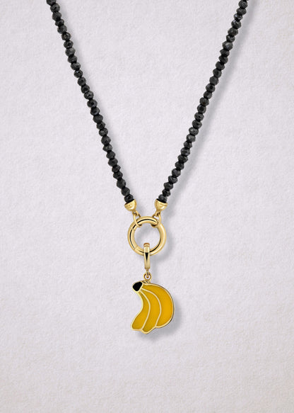 Close-up of the Noir Elegance Banana Bliss Charm Necklace, featuring faceted black spinel beads, a golden link charm holder, and a banana bliss charm with yellow enamel by whywhy NYC.