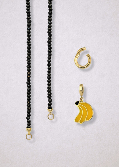Close-up of the separated Noir Elegance Banana Bliss Charm Necklace components: faceted black spinel necklace, golden link charm holder, and banana bliss charm with yellow enamel by whywhy NYC.