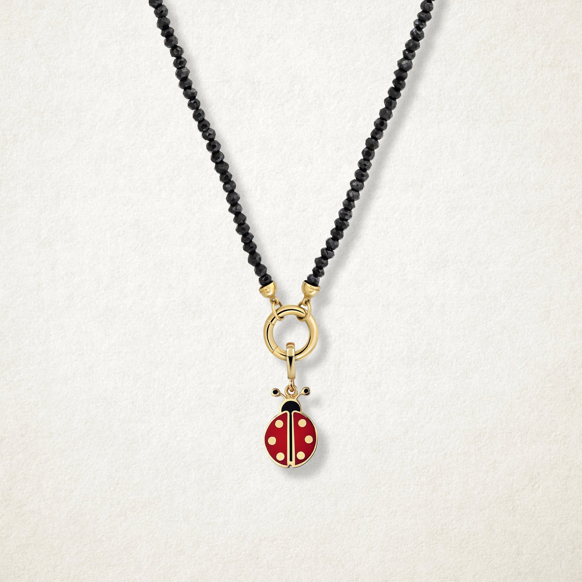 Close-up of the Lucky Ladybird Charm with red and black enamel on the Noir Elegance black spinel bead necklace, shown on a soft light background.