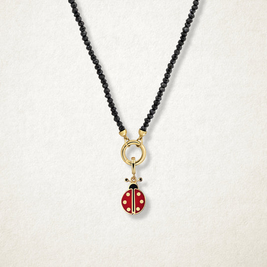 Close-up of the Lucky Ladybird Charm with red and black enamel on the Noir Elegance black spinel bead necklace, shown on a soft light background.