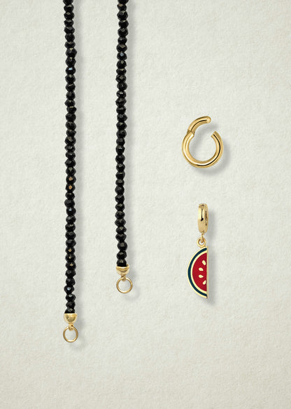 Close-up of the separated Noir Elegance Watermelon Wonder Charm Necklace components: black spinel necklace, golden link charm holder, and watermelon wonder charm with pink and green enamel by whywhy NYC.