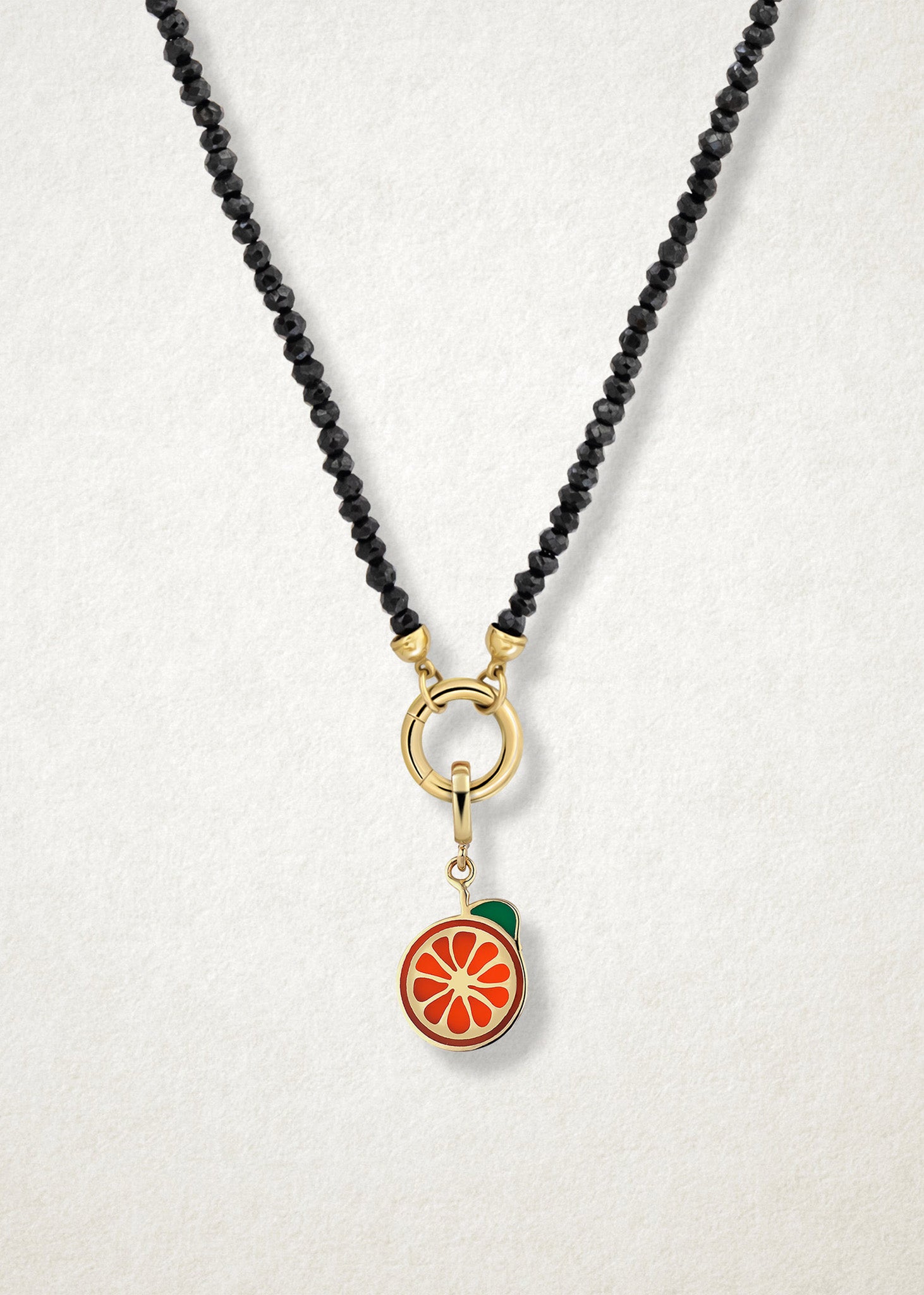 Close-up of the Orange Crush Charm paired with the Noir Elegance Charm Necklace by whywhy NYC, featuring black spinel and 14K solid gold for a bold and citrus-inspired style.