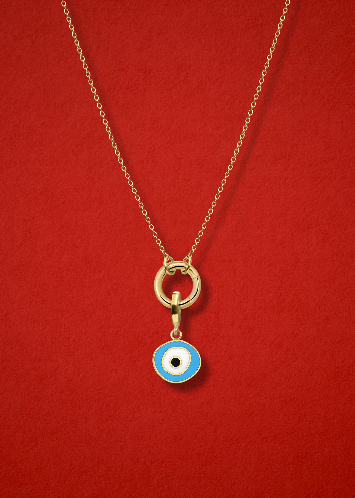 Close-up of the Sky Organic Evil Eye Charm with hand-painted enamel on a 14K solid gold cable chain necklace, shown on a red background.