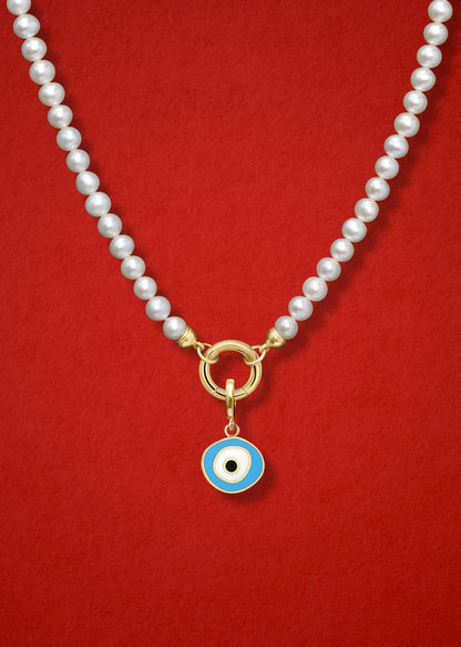 Close-up of the Sky Organic Evil Eye Charm with sky blue, white, and black enamel on the Lustrous Pearl necklace, shown on a red background.