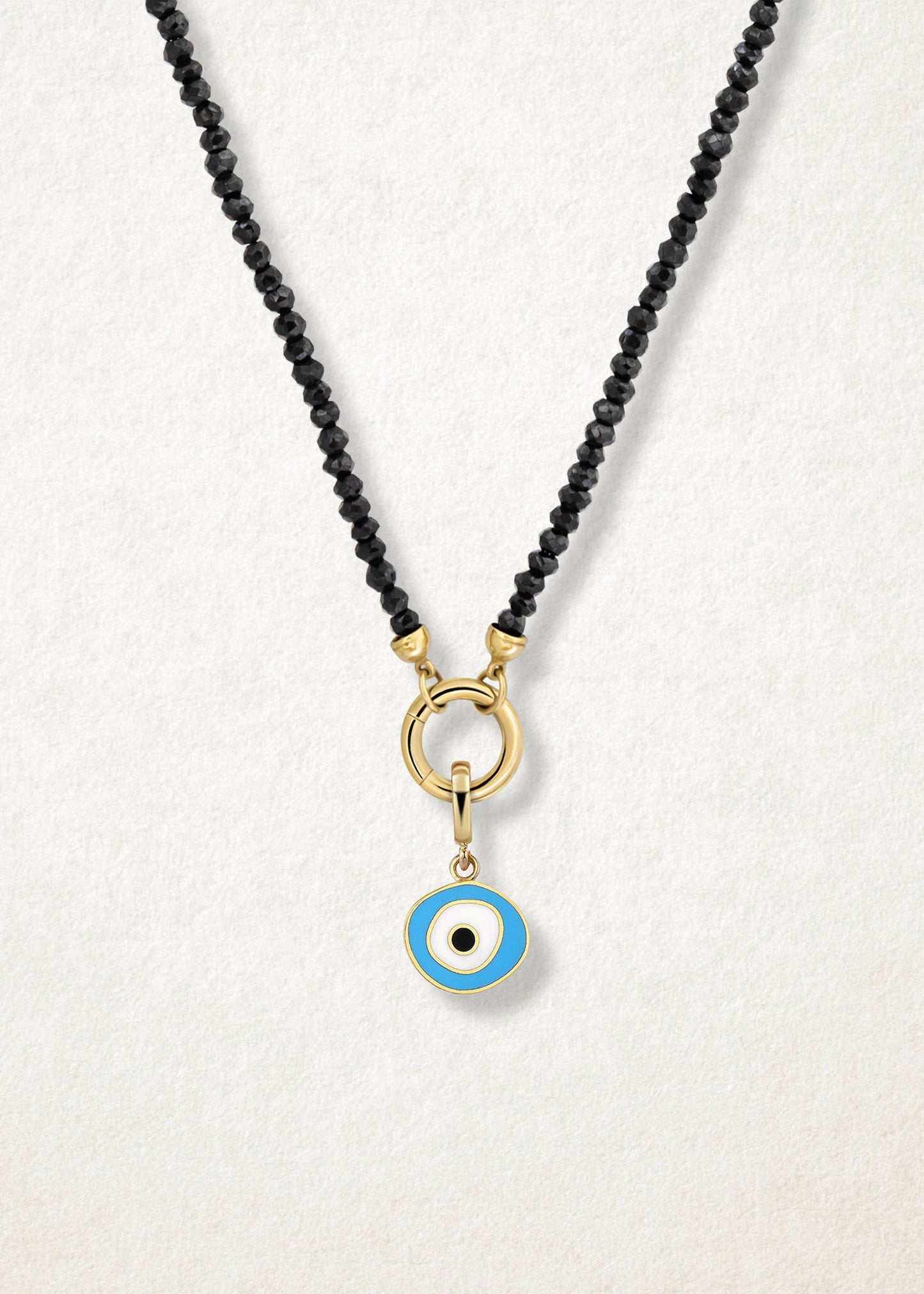 Close-up of the Sky Organic Evil Eye Charm with sky blue, white, and black enamel on the Noir Elegance black spinel bead necklace, shown on a soft light background.