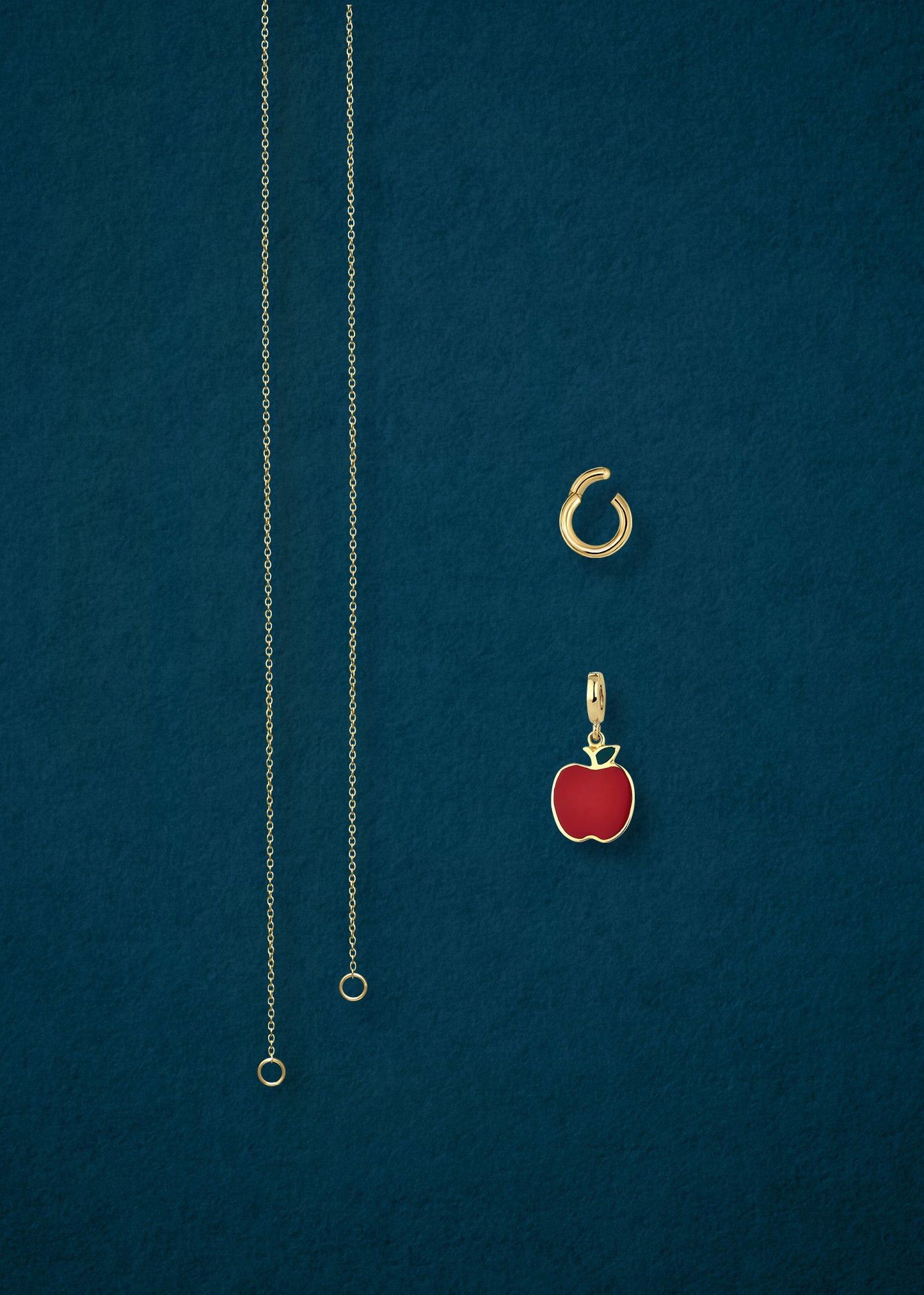 Separated components of the Golden Grace Apple Charm Necklace, including 14K solid gold cable chain, golden link charm holder, and golden apple of NYC charm with red enamel by whywhy NYC.