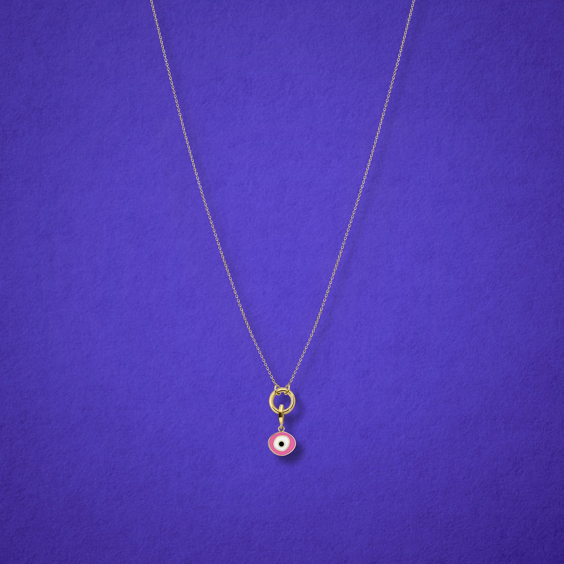 Blush Organic Evil Eye Charm with pink, white, and black enamel shown on the Golden Grace cable chain necklace for scale on a lilac background.