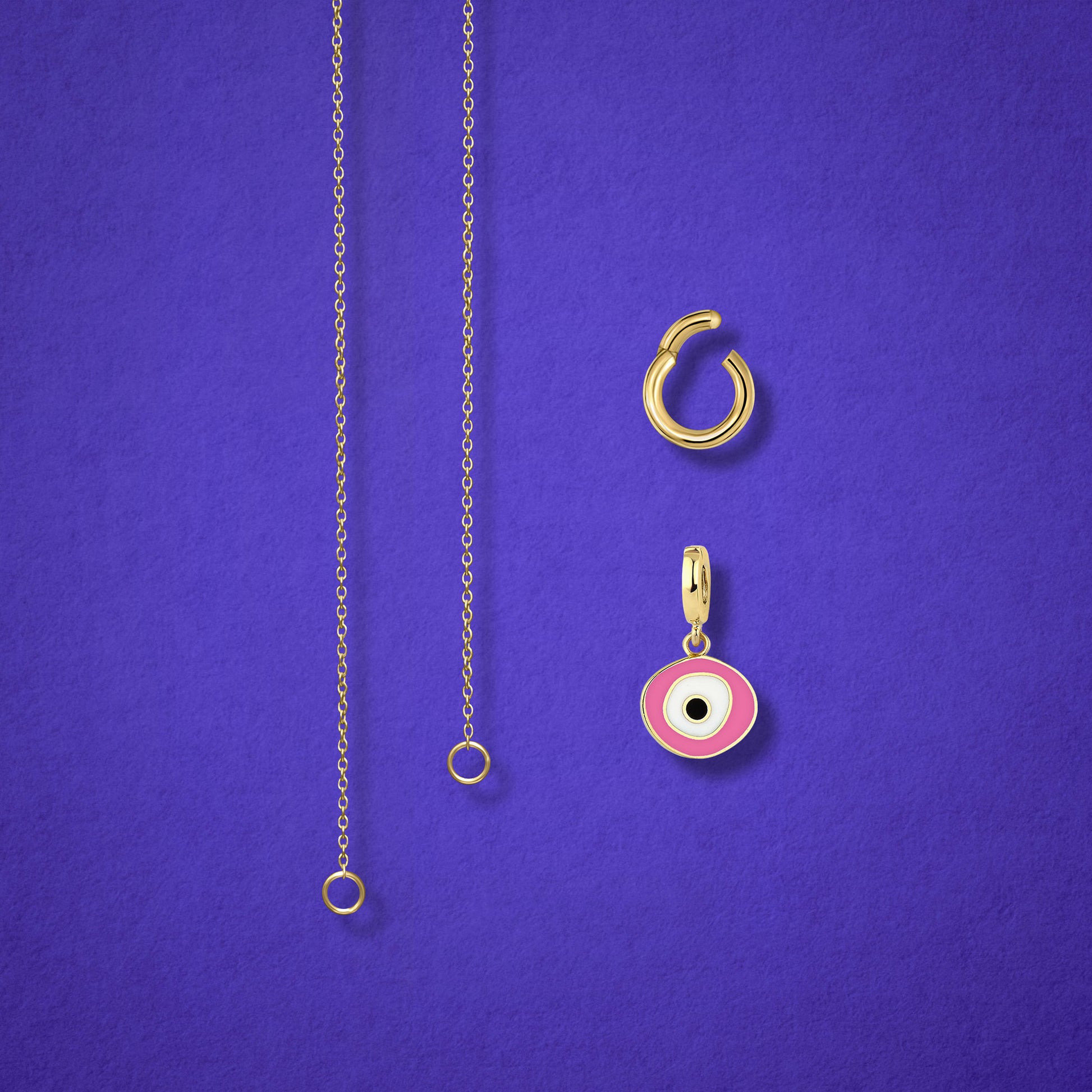 Close-up of the Blush Organic Evil Eye clip-on charm and Golden Link Charm Holder displayed side by side with the Golden Grace cable chain necklace on a lilac background.