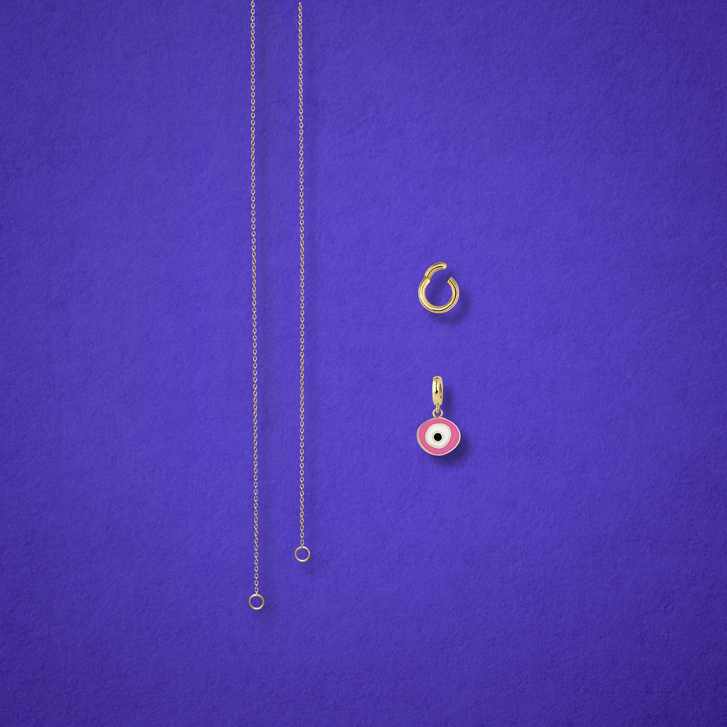 Blush Organic Evil Eye Charm, Golden Link Charm Holder, and the Golden Grace cable chain necklace displayed separately on a lilac background to show styling options.