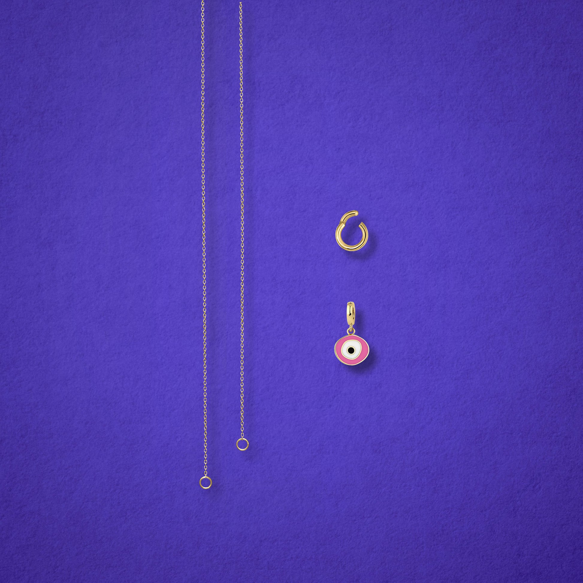 Blush Organic Evil Eye Charm, Golden Link Charm Holder, and the Golden Grace cable chain necklace displayed separately on a lilac background to show styling options.
