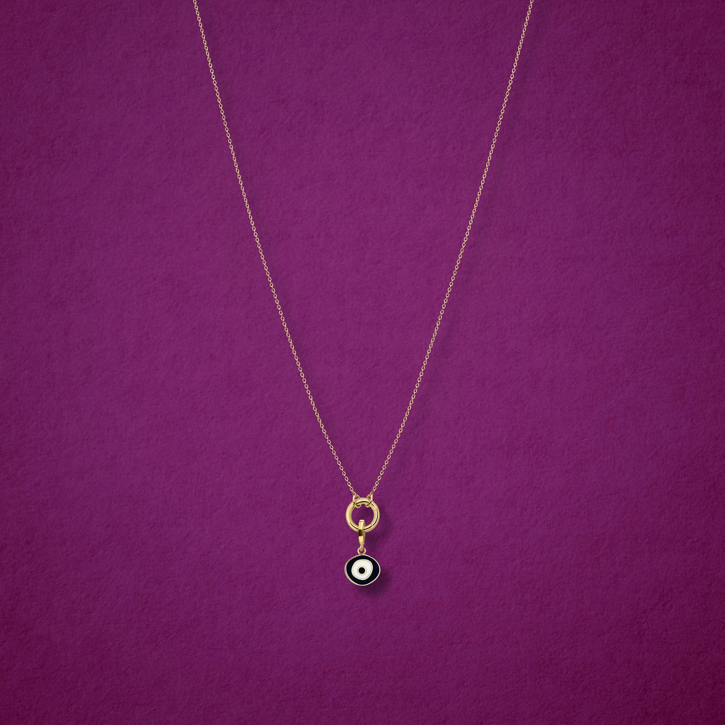 Obsidian Organic Evil Eye Charm with black and white enamel shown on the Golden Grace cable chain necklace for scale on a magenta background.