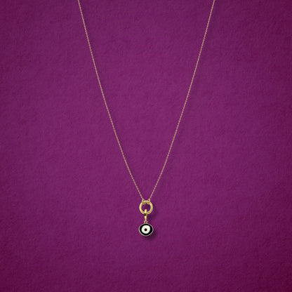 Obsidian Organic Evil Eye Charm with black and white enamel shown on the Golden Grace cable chain necklace for scale on a magenta background.