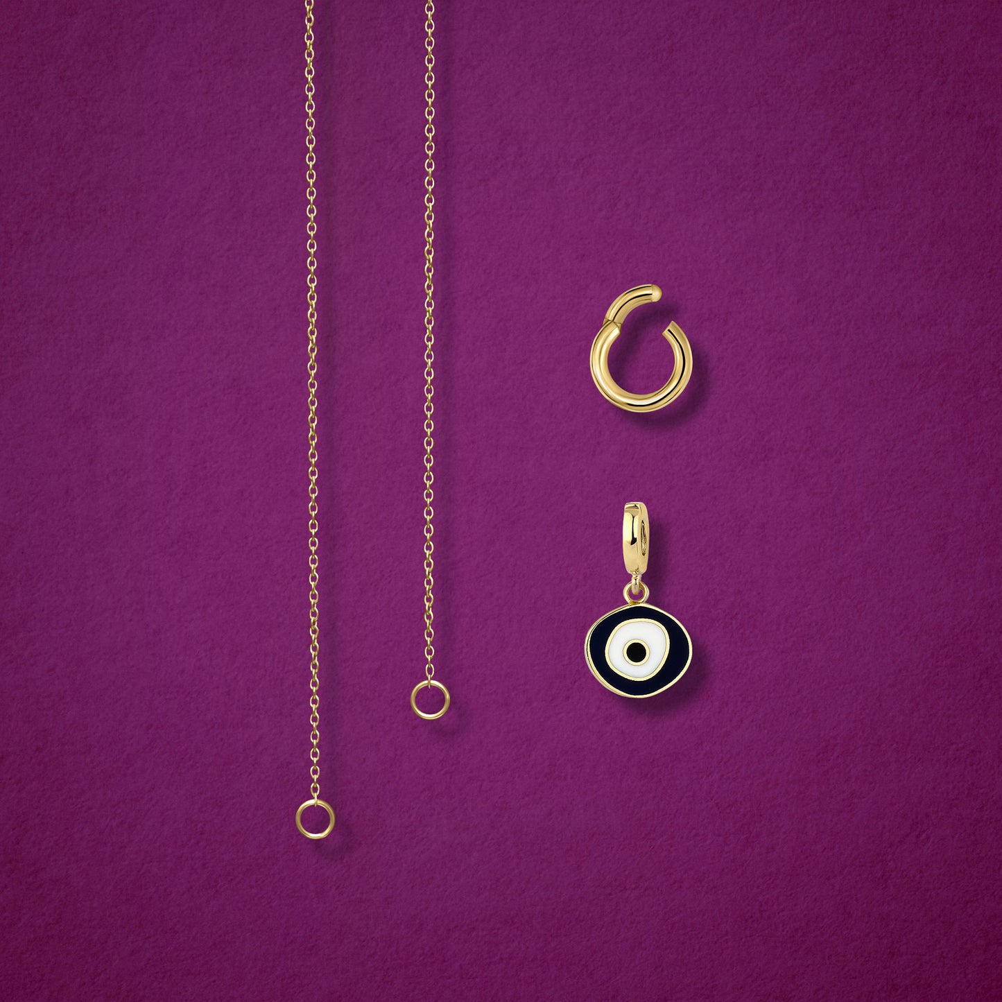 Close-up of the Obsidian Organic Evil Eye clip-on charm and Golden Link Charm Holder displayed side by side with the Golden Grace cable chain necklace on a magenta background.