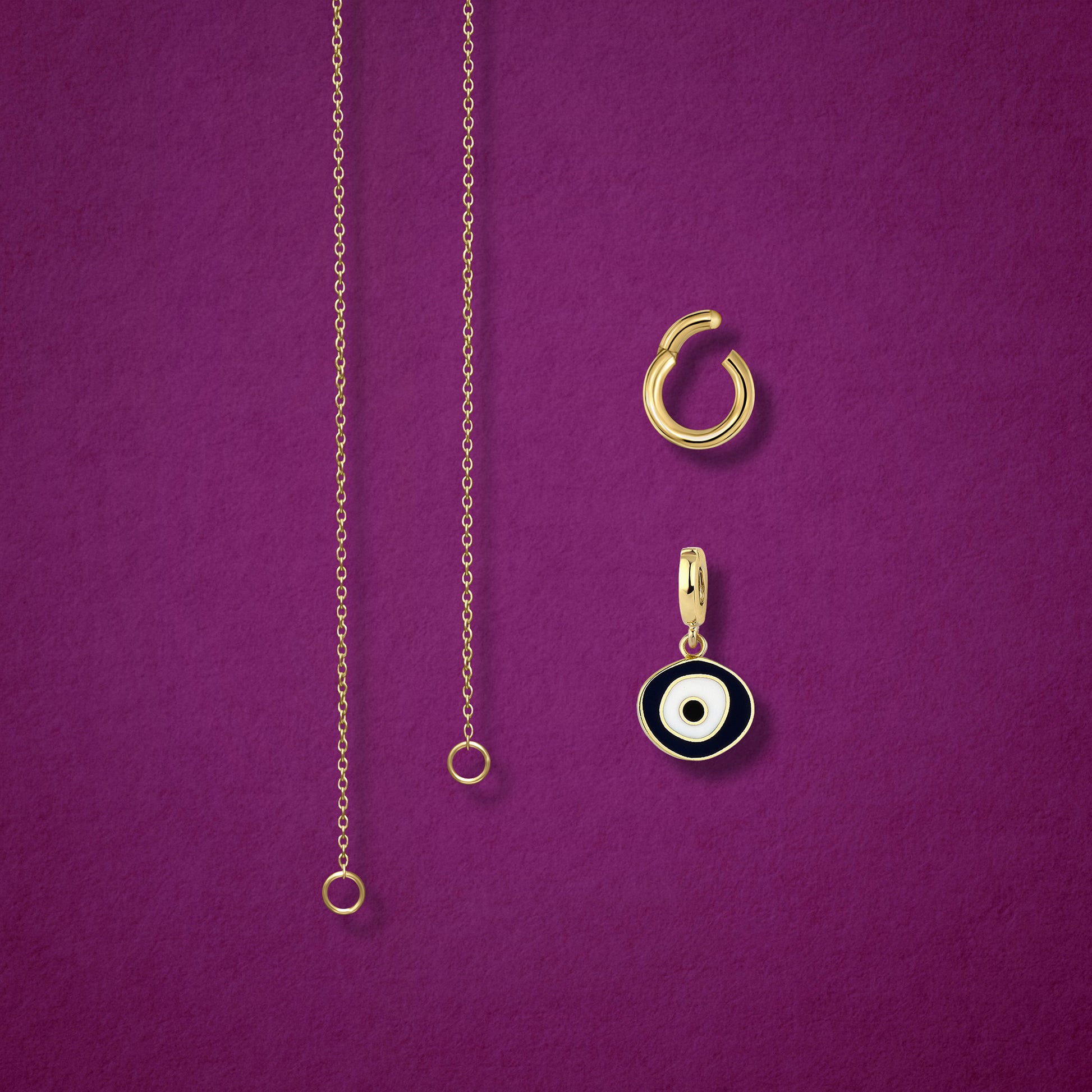 Close-up of the Obsidian Organic Evil Eye clip-on charm and Golden Link Charm Holder displayed side by side with the Golden Grace cable chain necklace on a magenta background.
