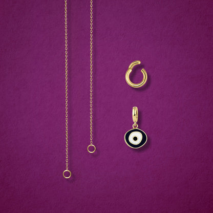 Close-up of the Obsidian Organic Evil Eye clip-on charm and Golden Link Charm Holder displayed side by side with the Golden Grace cable chain necklace on a magenta background.