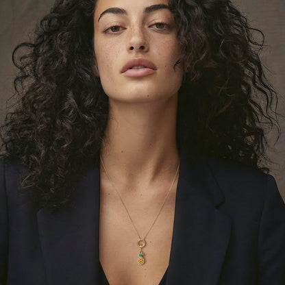 Model wearing the Golden Grace Pineapple Paradise Charm Necklace, featuring a 20-inch 1.5mm cable chain, an 11mm outer diameter, a 1.5mm thick 14K solid gold charm holder, and a green and yellow enamel pineapple charm crafted in 14K solid gold.