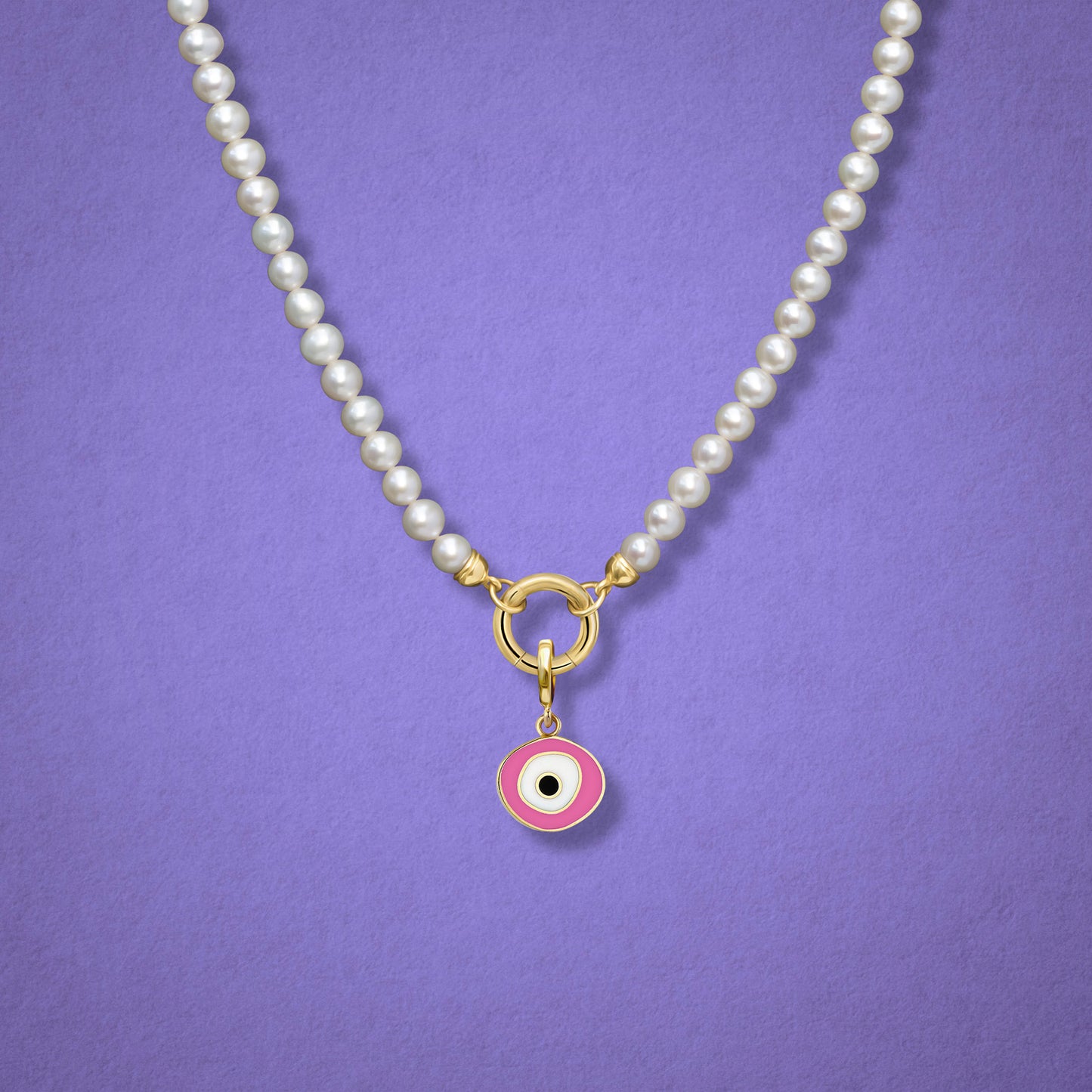 Close-up of the Blush Organic Evil Eye Charm with pink, white, and black enamel on the Lustrous Pearl necklace, shown on a lilac background.