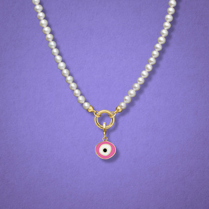 Close-up of the Blush Organic Evil Eye Charm with pink, white, and black enamel on the Lustrous Pearl necklace, shown on a lilac background.