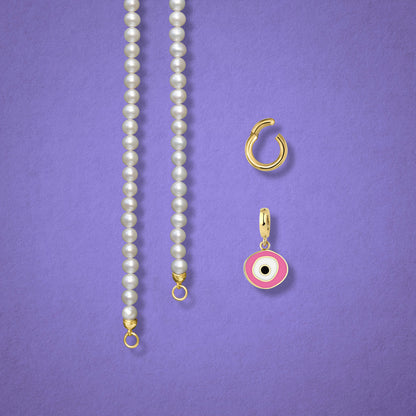 Close-up of the Blush Organic Evil Eye clip-on charm, Golden Link Charm Holder, and the Lustrous Pearl necklace displayed side by side on a lilac background.