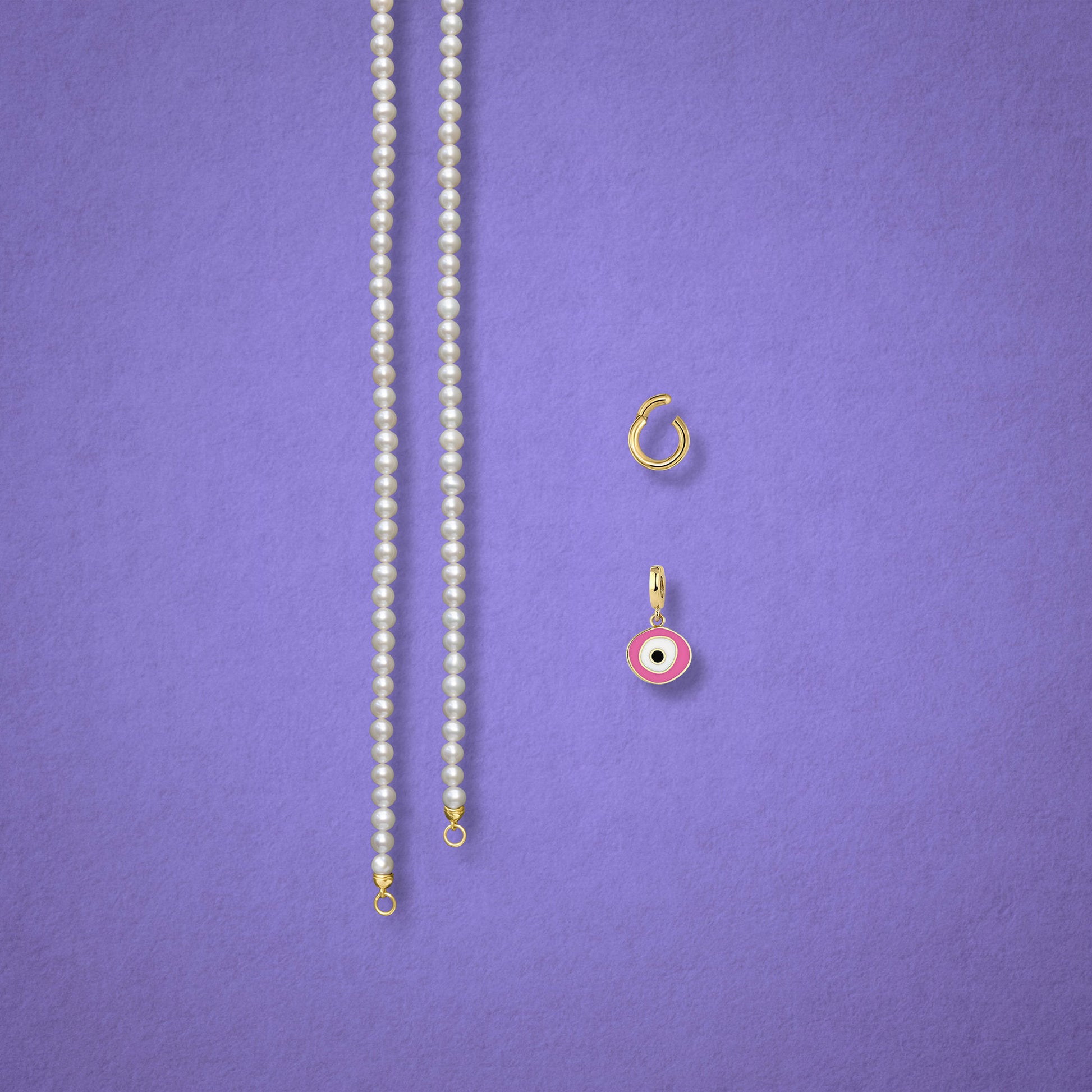 Blush Organic Evil Eye Charm, Golden Link Charm Holder, and the Lustrous Pearl necklace displayed separately on a lilac background to show styling options.
