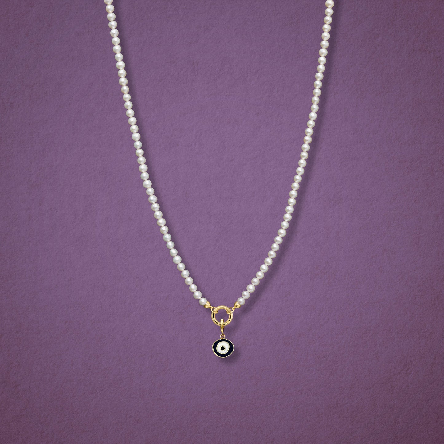Obsidian Organic Evil Eye Charm with black and white enamel shown on the Lustrous Pearl necklace for scale on a pink background.
