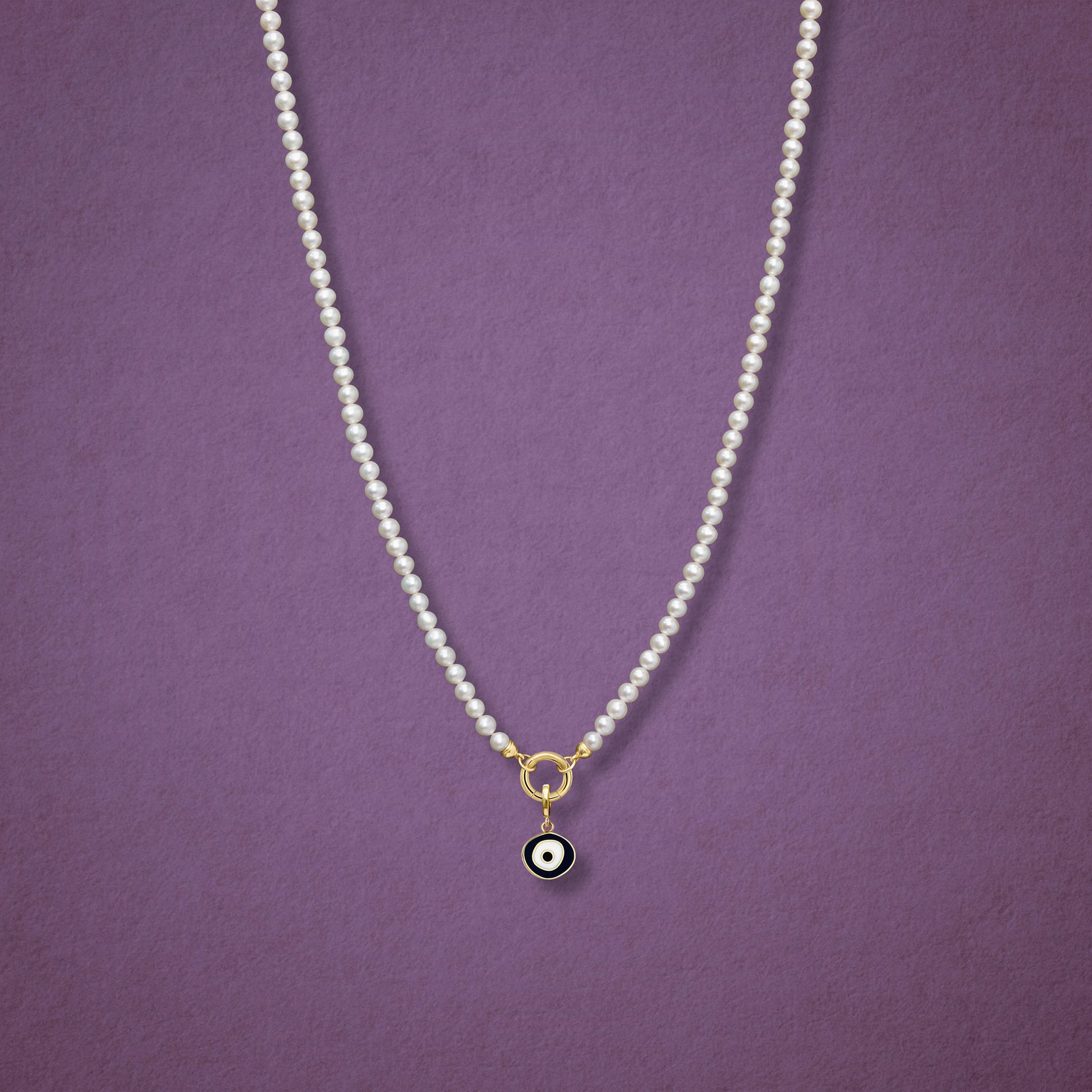 Obsidian Organic Evil Eye Charm with black and white enamel shown on the Lustrous Pearl necklace for scale on a pink background.